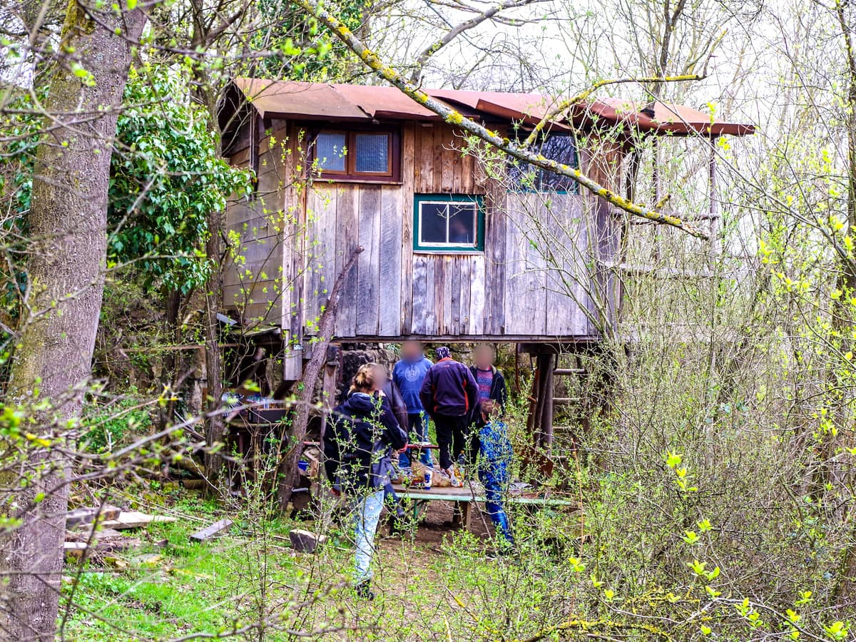 Ein Baumhaus aus Holz zwischen Bäumen, davor eine kleine Gruppe
