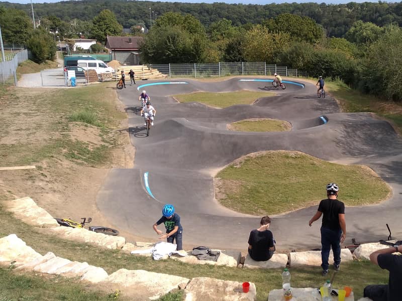 Kinder fahren mit dem Rad über die Wellen eines Pumptracks, am Rand schauen andere zu