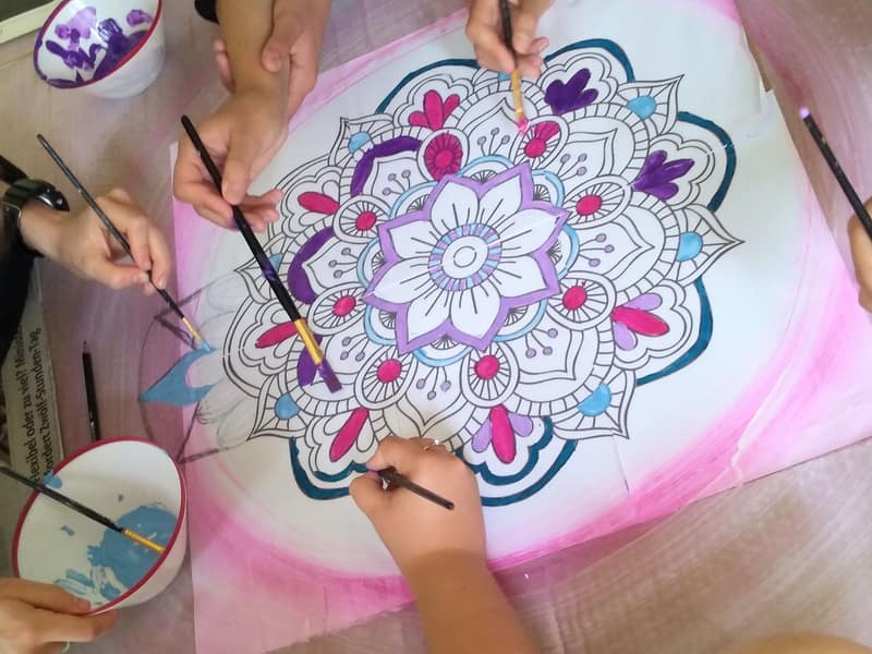 Mehrere Hände malen gemeinsam ein großes Mandala aus